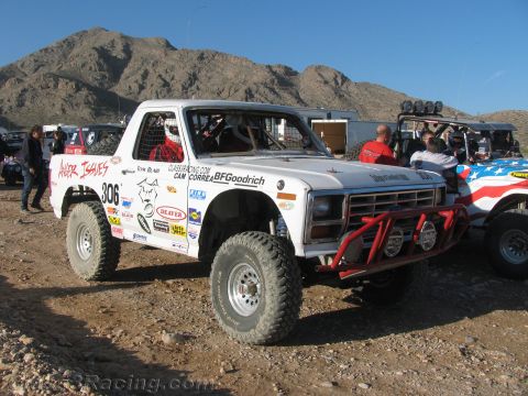 1990 Ford Bronco - white number 306 full-size Ford Bronco off-road racer covered in sponsor decals sits in a rocky desert pit area.