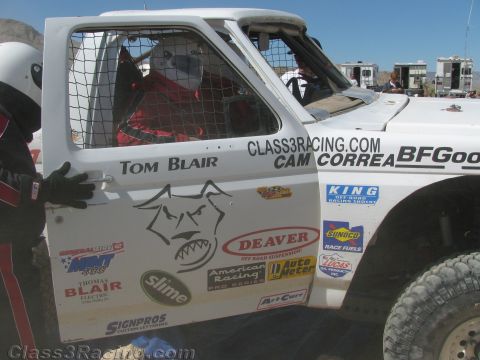 1990 Ford Bronco - white door of an off-road race truck lettered "Tom Blair" and "Cam Correa" with Deaver and other sponsor decals and a dog-face logo.