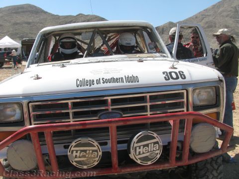 1990 Ford Bronco - front of a white Ford race truck numbered 306, lettered "College of Southern Idaho," with a red brush guard and twin Hella lights.