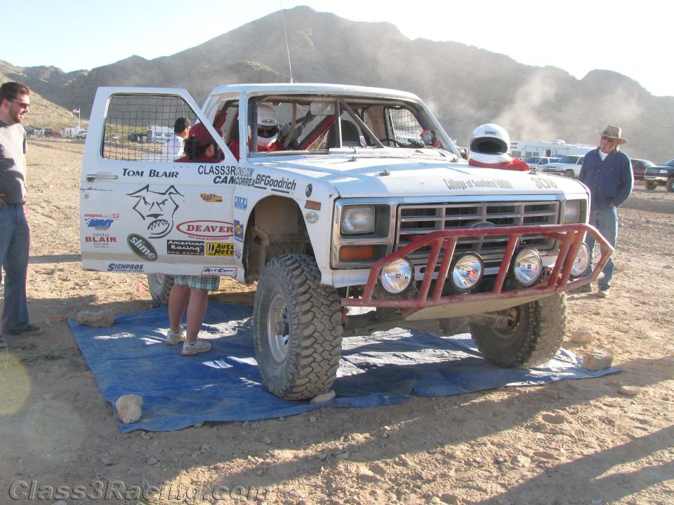 White off-road race truck with red tube bumper and round lights in desert pit