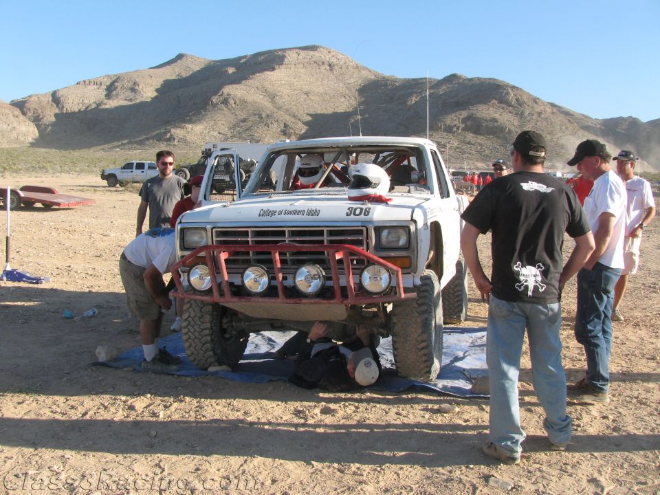 White race truck number 306 with red bumper, people gathered around in desert