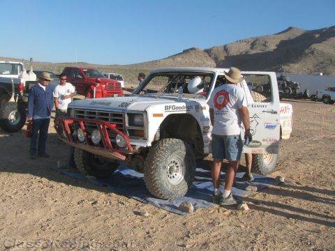 1990 Ford Bronco - crew member tends the rear of a white off-road race truck numbered 306 with a red bumper in a desert pit.