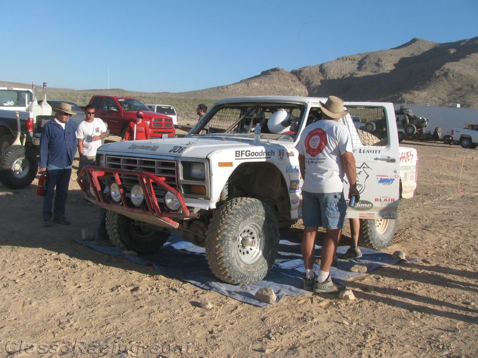 White off-road race truck number 306 in desert pit with crew refueling