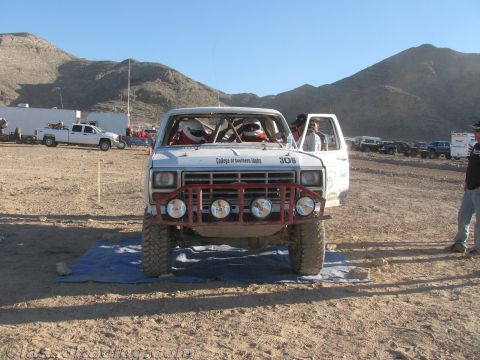 1990 Ford Bronco - Head-on view of a white desert race truck numbered 306 with a red grille guard and round driving lights, parked on a tarp.