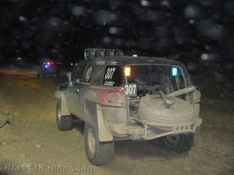 1990 Ford Bronco - dusty off-road race truck numbered 307 with a rear-mounted spare tire and Toyota decal sits on a dark desert course.