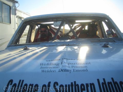 1990 Ford Bronco - Two helmeted occupants sit inside a roll-caged race truck whose body reads College of Southern Idaho with welding credits.
