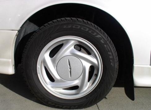 Silver alloy wheel with Thunderbird center cap and Goodyear tire on white car