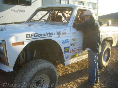 1990 Ford Bronco - person leans into the cab of a white off-road race truck numbered 66 with BFGoodrich and Deaver decals in a desert pit.