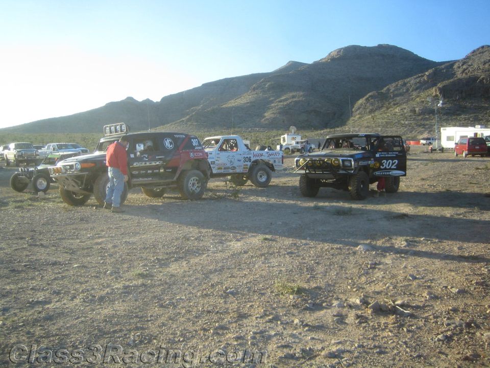 Row of off-road race trucks including white 306 and blue 302 in desert