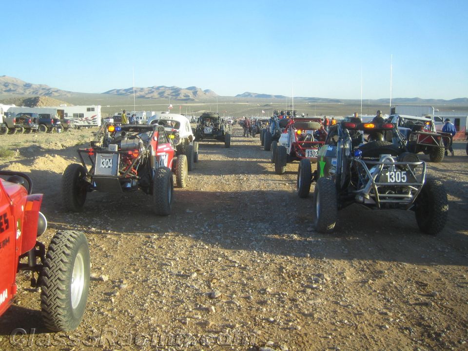 Many off-road buggies including 1304 and 1305 staged on gravel in desert