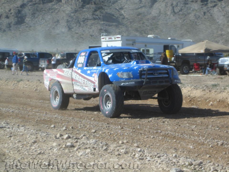 Blue and red off-road race truck no. 906 jumping on dirt at a desert race
