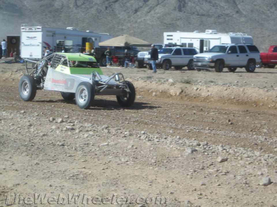 Green and white tube-frame off-road buggy on a dirt course with trailers behind