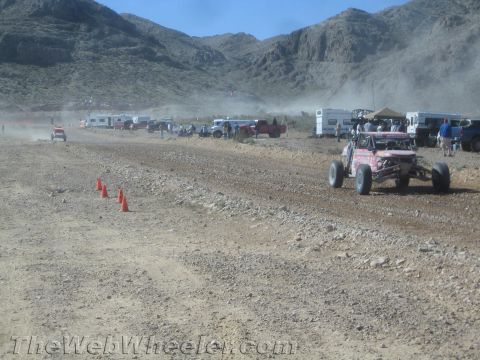 1990 Ford Bronco - Off-road race vehicles and a pink buggy line a cone-marked dirt course in a dusty desert valley ringed by mountains.