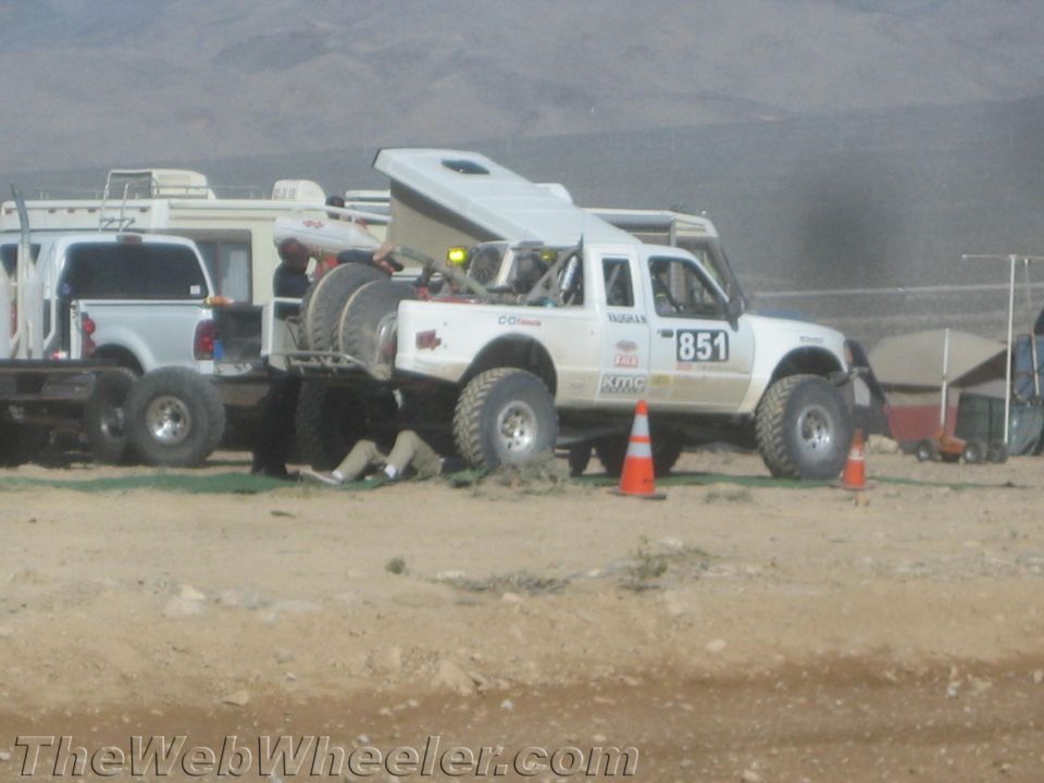 White race truck no. 851 in a desert pit with hood open and crew working
