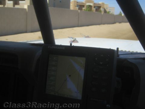 1990 Ford Bronco - Lowrance GPS unit on a roll-caged dash shows a map screen, with a walled sandy lot visible beyond the windshield.