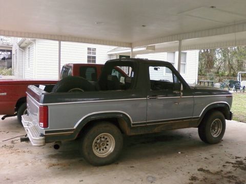 1983 Ford Bronco - Side view of a two-tone gray and black Ford Bronco parked under a carport.