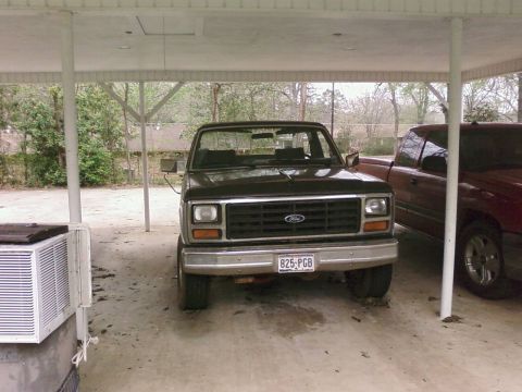 1983 Ford Bronco - This black Ford truck, likely from the early 1980s, is parked under a carport next to another vehicle.