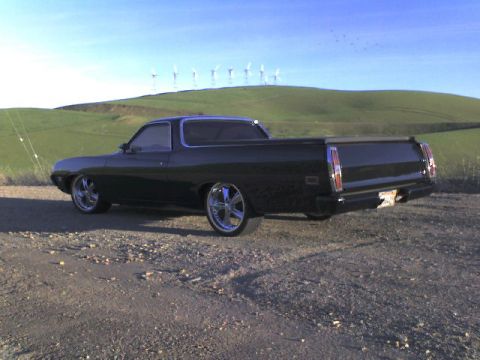 1970 Ford Ranchero - A black 1970 Ford Ranchero pickup truck is parked on a dirt road with rolling hills and windmills in the background.