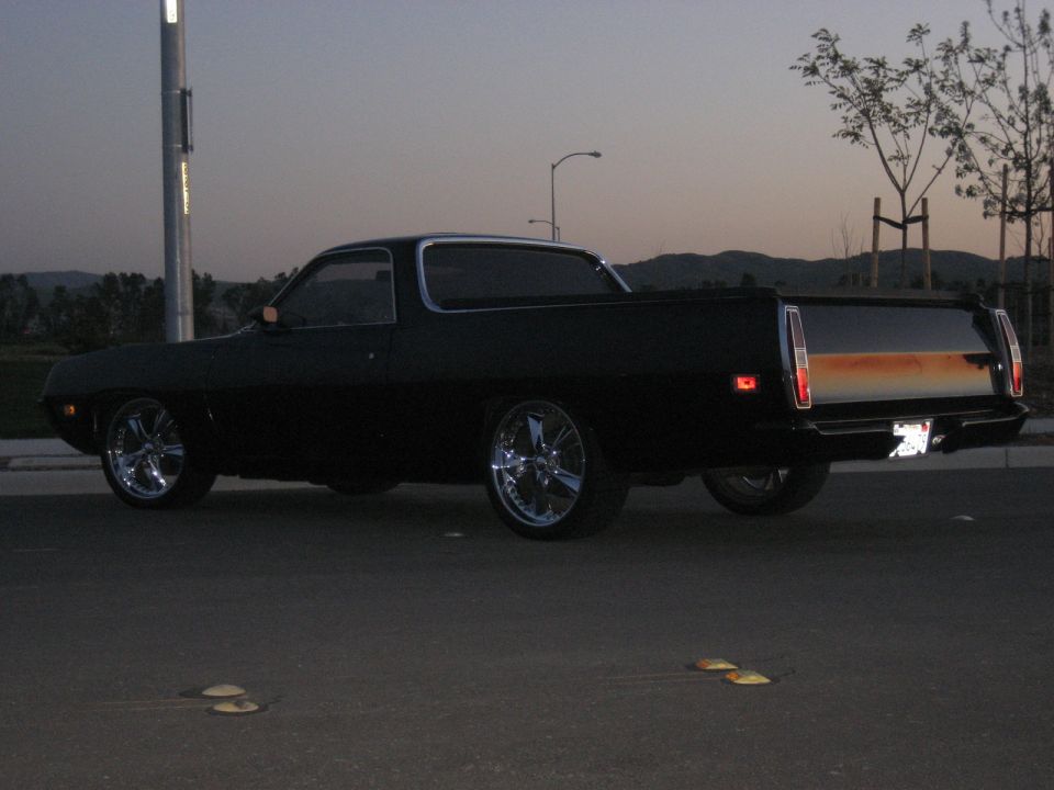 Black coupe-utility with bed and chrome five-spoke wheels, rear 3/4 view at dusk