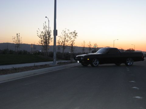 1970 Ford Ranchero - A black 1970 Ford Ranchero is parked on a street during sunset, its chrome wheels.