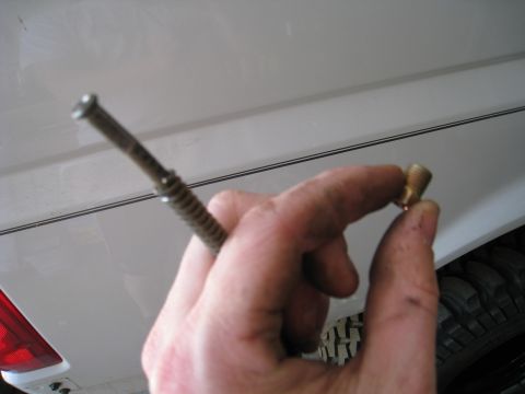 1996 Ford Bronco - A person holds a small brass fitting and a metal rod, with a vehicle's body and tire visible in the background.