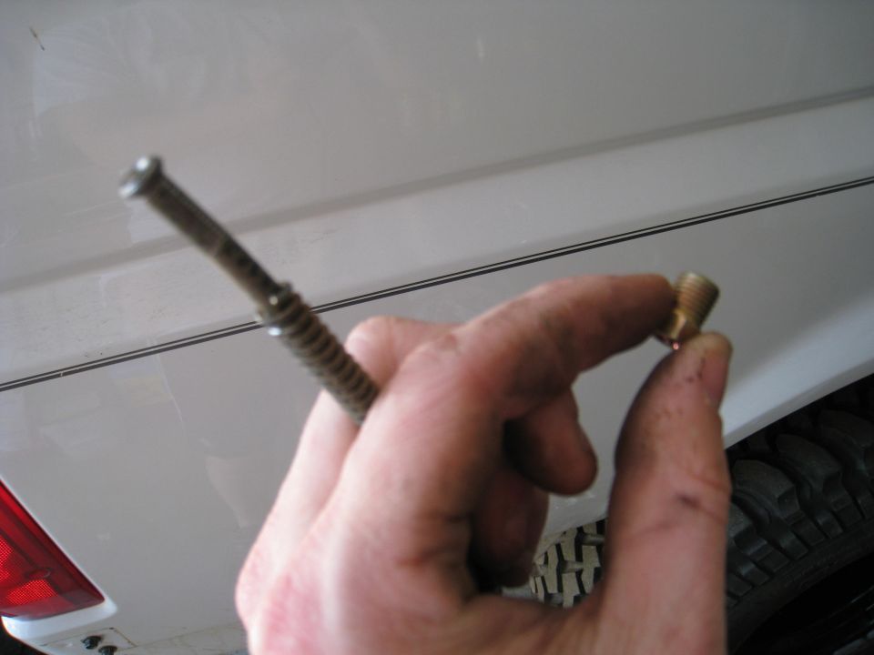 Hand holding a small brass fitting and a metal rod with a screw head