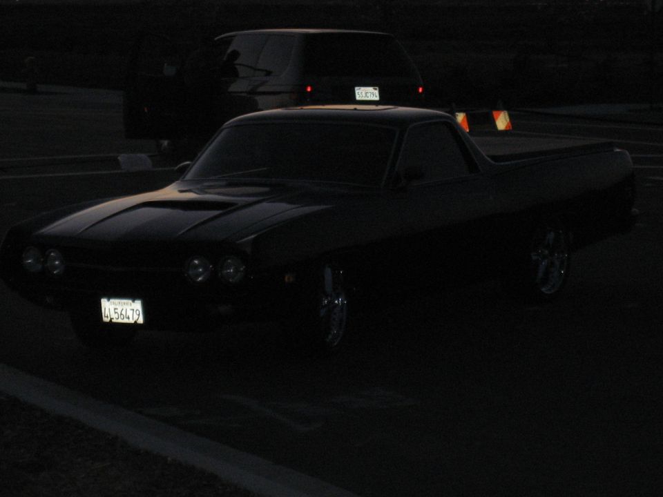 Black Ranchero car-pickup, 3/4 front view, chrome wheels, CA plate, parked at dusk