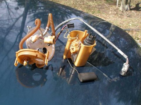 1997 Ford Taurus - A disassembled fuel pump assembly, including hoses and electrical connectors, rests on a dark, reflective surface.
