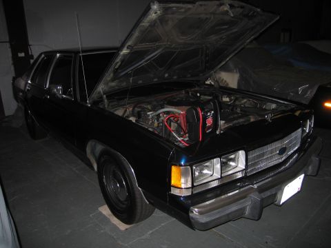 1991 Ford LTD Crown Victoria - The front of a dark blue sedan is shown with its hood open, revealing the engine compartment.