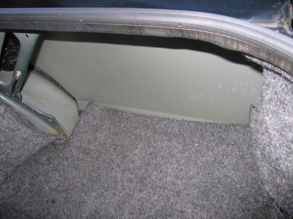 Interior of a car trunk with gray carpet lining and painted metal panels