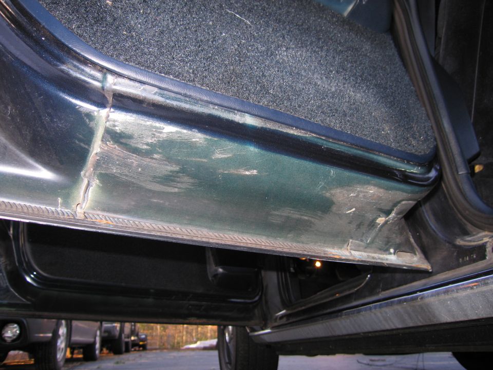 Close-up of a car's interior door sill with scuff marks and worn carpet