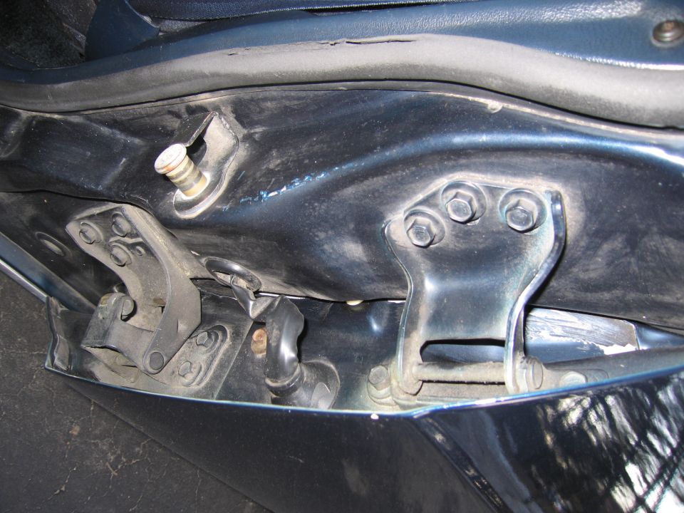 Close-up of a car door hinge assembly with bolts and a rubber seal