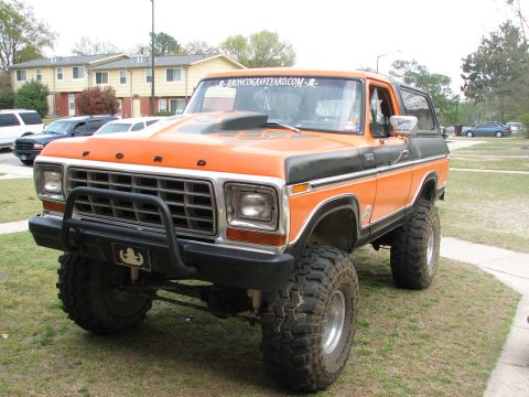 1979 Ford Bronco - Orange and black 1978-1979 Ford Bronco with brush guard, lifted on mud tires, parked on grass at a show.