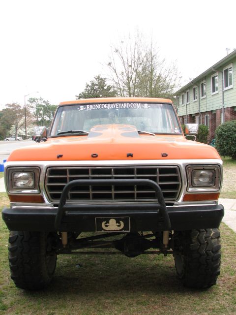 1979 Ford Bronco - Head-on view of a lifted orange late-1970s Ford truck with FORD block letters across the hood, dual rectangular headlights, a chrome egg-cr…
