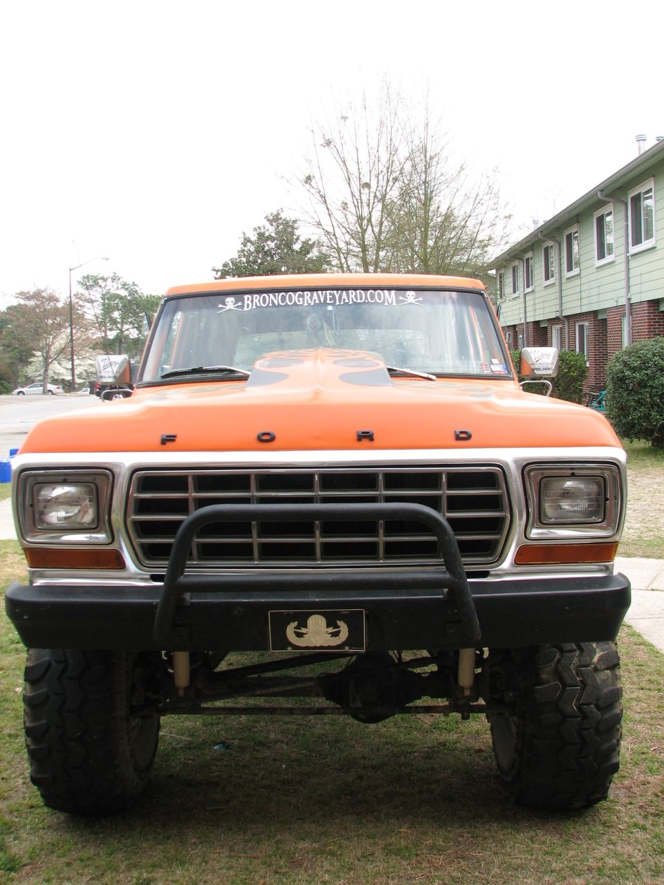 Lifted orange late-1970s Ford truck front view with bull bar and windshield banner