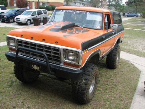 1979 Ford Bronco - A lifted orange first-generation-style Ford Bronco with black flame graphics, black hardtop, and large off-road tires on white steel wheels…