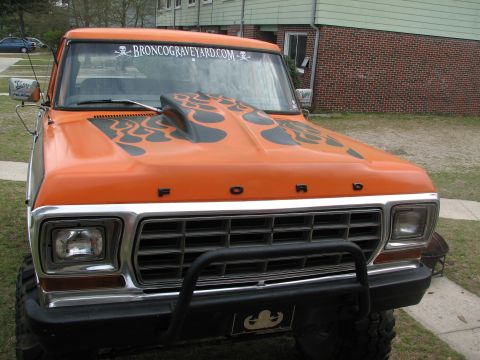 1979 Ford Bronco - Front three-quarter view of an orange Ford Bronco with black flame graphics on the hood and 'FORD' lettering on the grille panel. The winds…