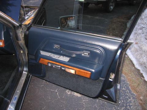 1991 Ford LTD Crown Victoria - Close-up of a car's interior door panel, showing blue vinyl and wood accents. Another vehicle is reflected in the window.