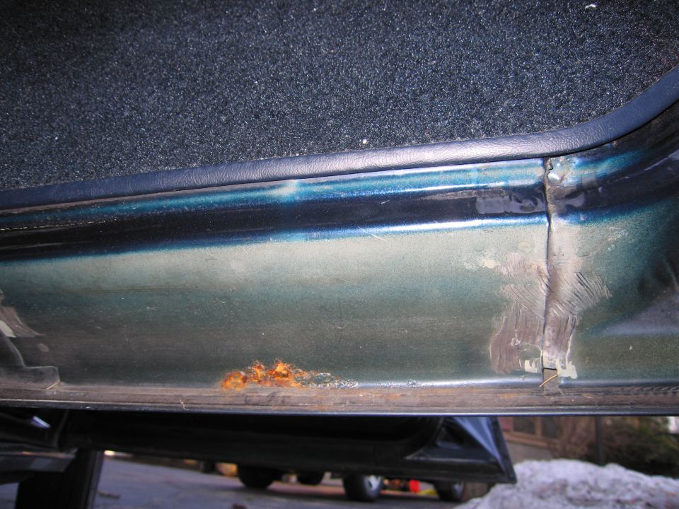 Green car door sill with rust and paint damage. Interior carpet visible above