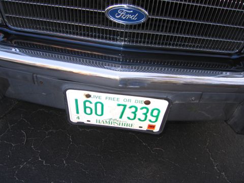 1991 Ford LTD Crown Victoria - Close-up of a Ford emblem on a chrome grille, with a New Hampshire license plate below.