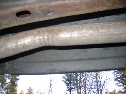 1991 Ford LTD Crown Victoria - Undercarriage detail showing exhaust pipe and frame, with trees in background.