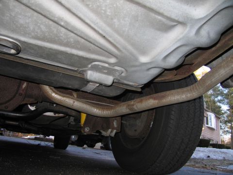 1991 Ford LTD Crown Victoria - A low-angle shot reveals the underside of a vehicle, focusing on the exhaust pipes, fuel tank, and a rear tire.