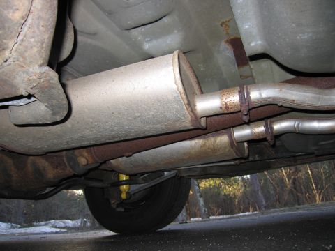 1991 Ford LTD Crown Victoria - The underside of a vehicle shows a dual exhaust system with mufflers and rusted pipes.