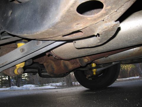 1991 Ford LTD Crown Victoria - The underside of a vehicle reveals a rusty frame, exhaust system, and yellow shock absorbers.