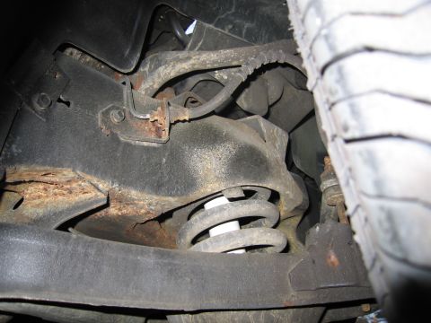 1991 Ford LTD Crown Victoria - Close-up of the front suspension system on a 1991 Ford Crown Victoria LTD, showing the coil spring and signs of rust on the frame component…