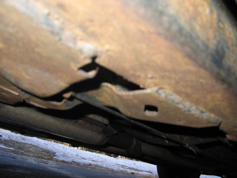 1991 Ford LTD Crown Victoria - The undercarriage of a vehicle displays extensive rust damage, with holes visible in the frame structure.