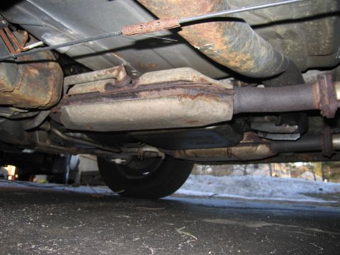 1991 Ford LTD Crown Victoria - The underside of a vehicle reveals a heavily rusted exhaust system and a portion of a tire.