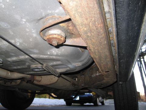 1991 Ford LTD Crown Victoria - The underside of a vehicle shows significant rust on its frame and suspension parts, with another car partially visible in the distance.