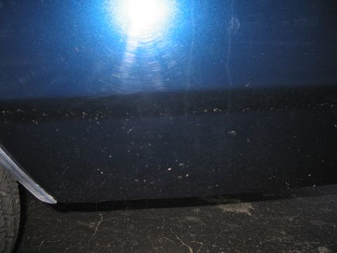 1991 Ford LTD Crown Victoria - The side of a blue vehicle shows dirt and swirl marks on the paint. A tire is visible on the left.