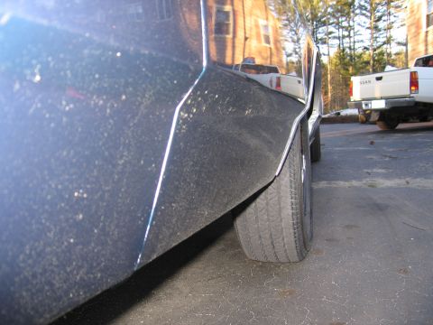 1991 Ford LTD Crown Victoria - Side view of a dark blue car's rear quarter panel and tire, with a white pickup truck visible in the background.